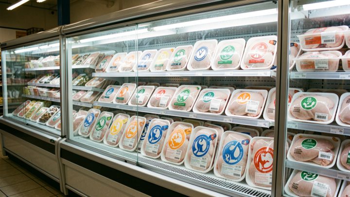 Rayon réfrigéré d’un supermarché français présentant des emballages de poulet différenciés par des symboles abstraits et des codes couleur évoquant le bien-être animal, sans marquages lisibles.